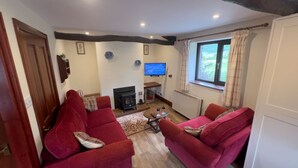 Una sala de estar acogedora con sofás rojos, una chimenea, un televisor y una ventana con cortinas.