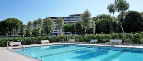 A rectangular swimming pool with a tiled deck, surrounded by greenery and benches.