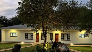Una casa moderna con un prato curato, un grande albero e due statue a forma di elefante.