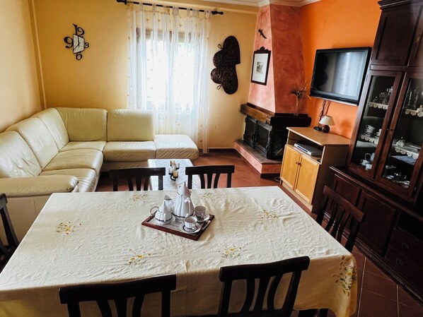 A living room with a sofa, dining table, chairs, a fireplace, and a television.