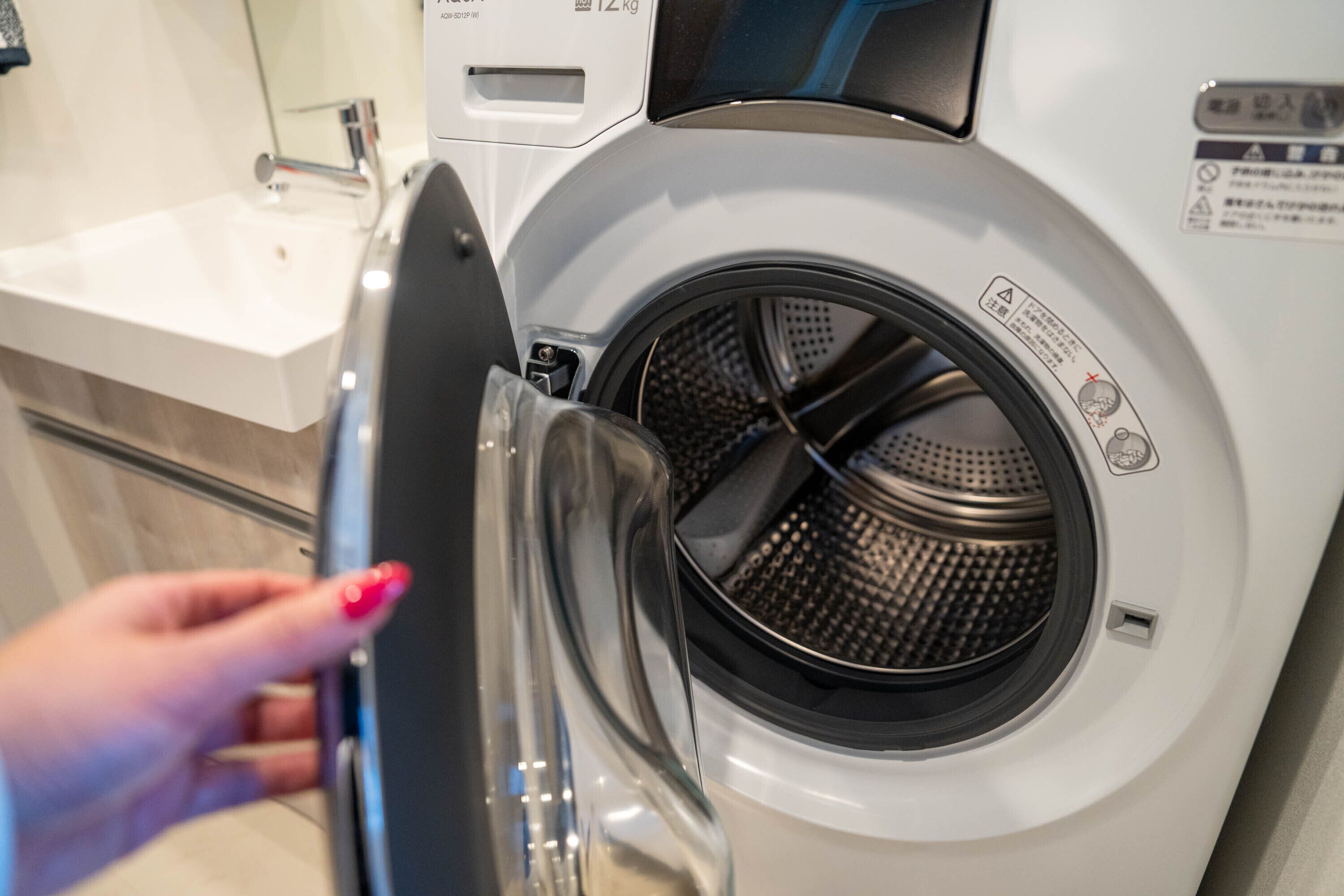 A front-loading washing machine with a transparent door, a control panel, and a warning label.