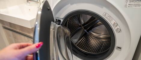 A front-loading washing machine with a transparent door, a control panel, and a warning label.