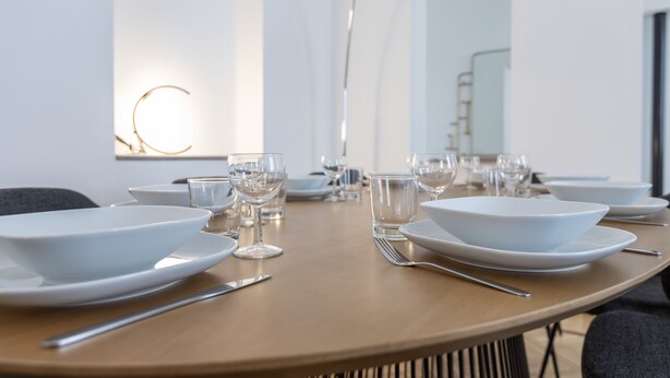 A dining table set with white plates, bowls, and clear glasses, with a modern lamp in the background.