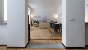A modern living room with a herringbone floor, a beige sofa, a dining table with chairs, and a wall mural.