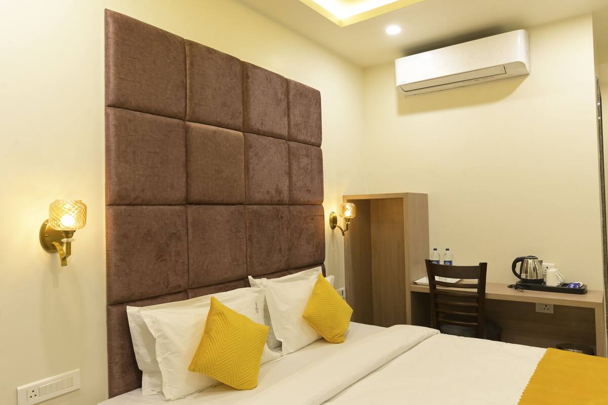 Ein Hotelzimmer mit hohem, gepolsterten Kopfteil, einem Schreibtisch mit Stuhl sowie einem Bett mit weißer und gelber Bettwäsche.