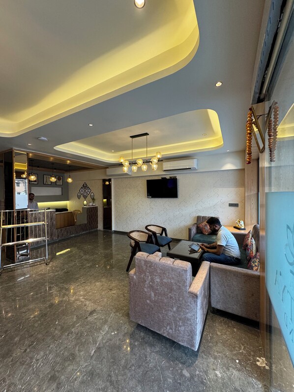A modern lobby with a marble floor, seating area with sofas and chairs, a reception desk, and a flat-screen TV mounted on the wall. - Hotel Aditya Grand - Bhopal (Bhopal)