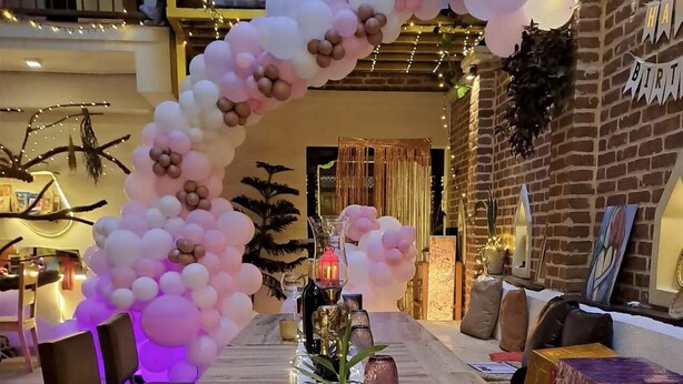 A long table with a white tablecloth, pink and white balloons, and decorative glassware. - Wittys hotel (Lalitpur)
