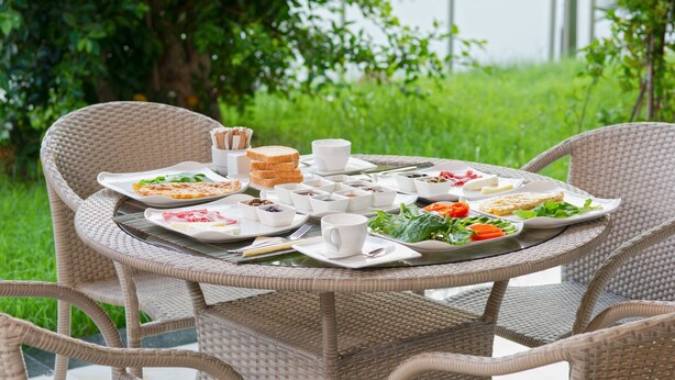 A round wicker table set outdoors with plates of food, bowls, and cups. - Citrus Luna Suite (Konyaalti)