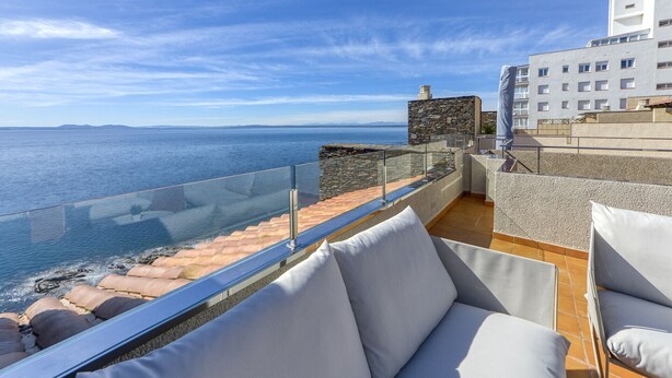 A terrace with a view of the sea, stone walls, and a building in the background. - DALLAS ATIC (Rosas / Roses)