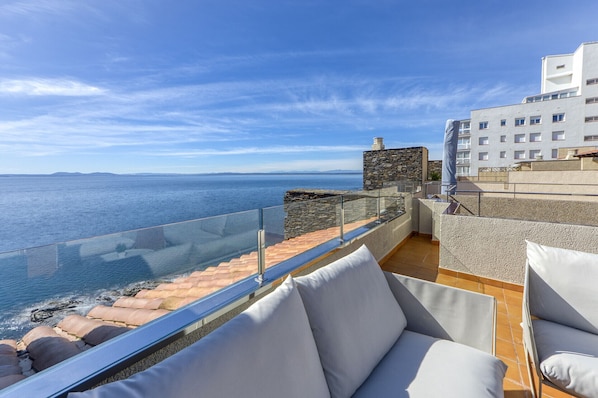 A terrace with a view of the sea, stone walls, and a building in the background.