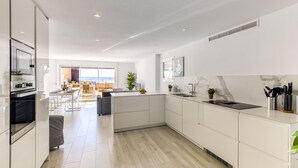 A modern kitchen with white cabinetry, a black stove, and a view to a balcony with outdoor seating. - DALLAS ATIC (Rosas / Roses)