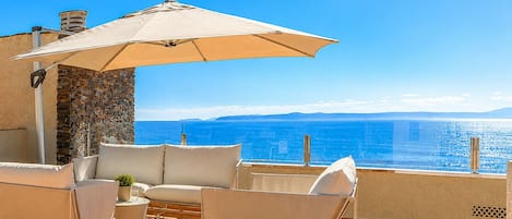 An outdoor seating area with a view of the sea, stone wall, and a pergola structure.