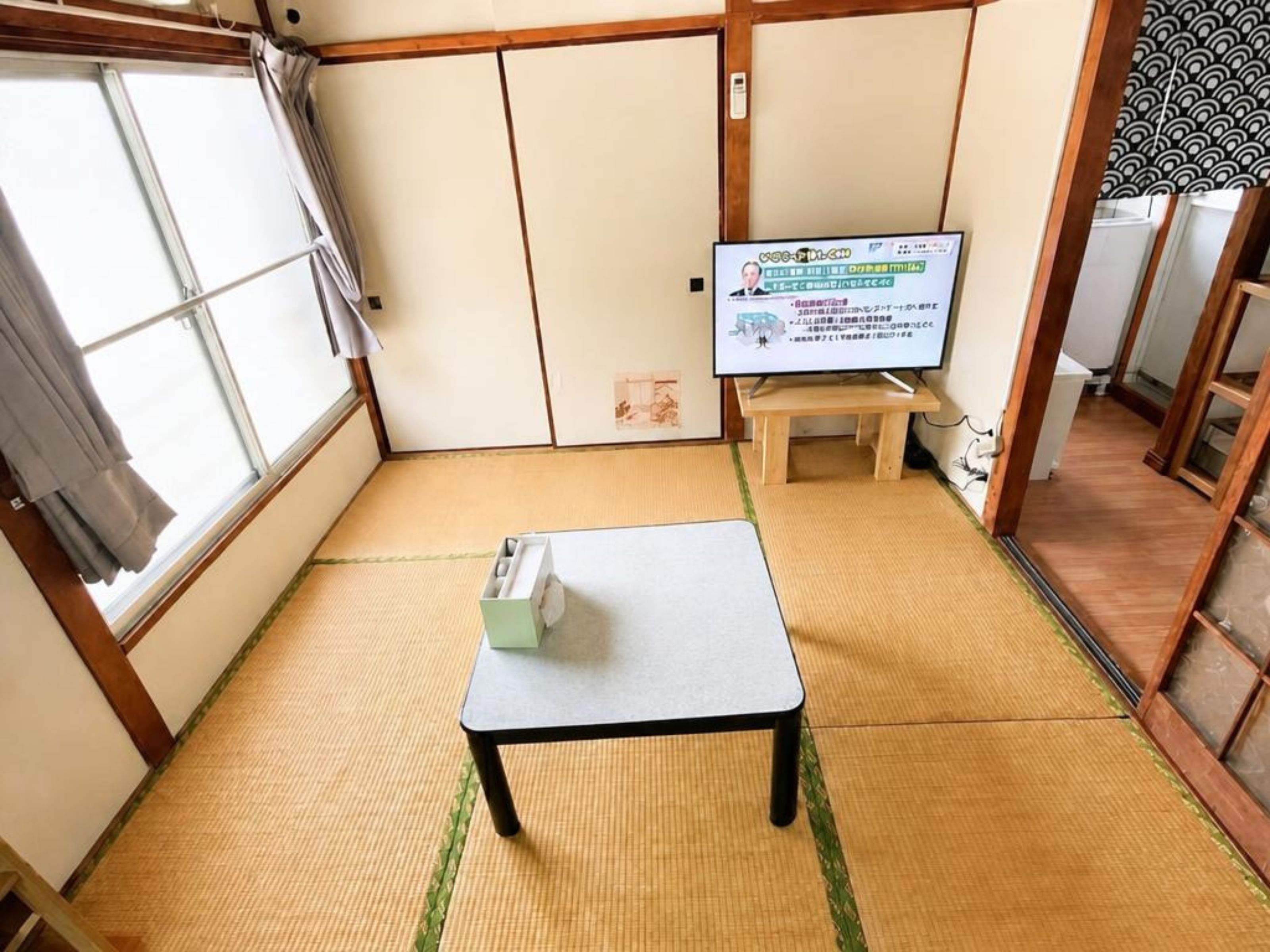 Een kamer met tatami matten, een televisie op een houten standaard, een klein tafeltje en schuifdeuren.
