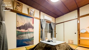A traditional Japanese-style living room with tatami flooring, a low table with a white object, and a large framed picture of a mountain scene.