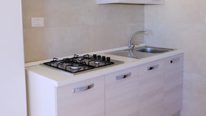 A compact kitchen with a gas stove, sink, and light-colored cabinets. - Casa Panorama Front of the Sea (Melendugno)