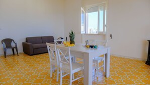 A dining area with a white table and chairs, a pineapple on the table, and a sofa in the background. - Casa Panorama Front of the Sea (Melendugno)
