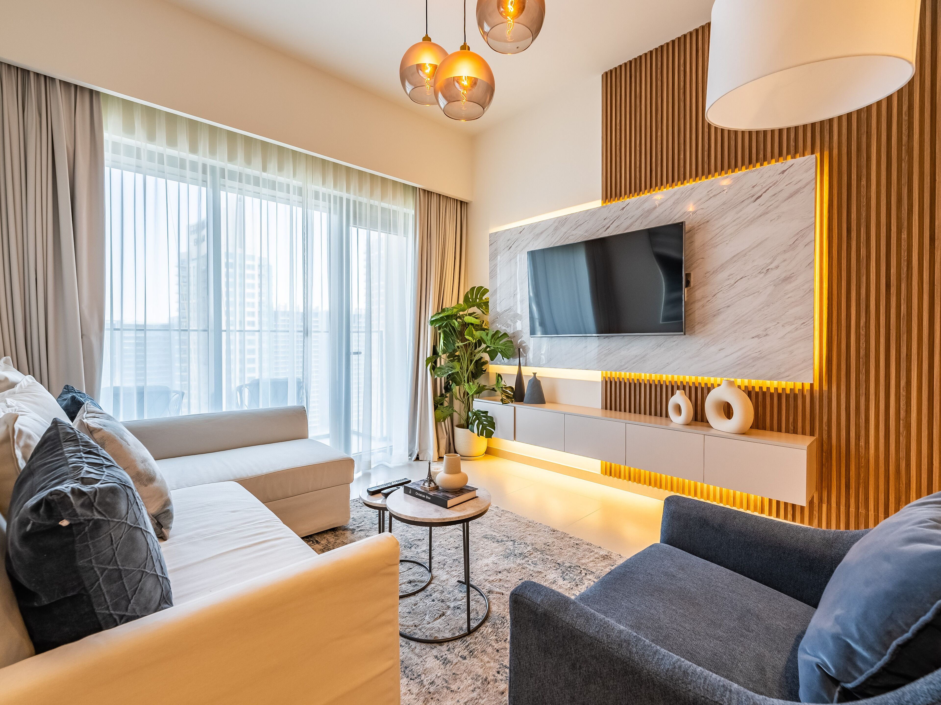 Un salon moderne avec un canapé, un fauteuil et un téléviseur fixé sur un mur en marbre.