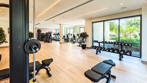A modern gym with cardio machines, free weights, and a large window offering a view of greenery. - Cityscape Splendor Lavish 1BR Uptown  (Dubai)