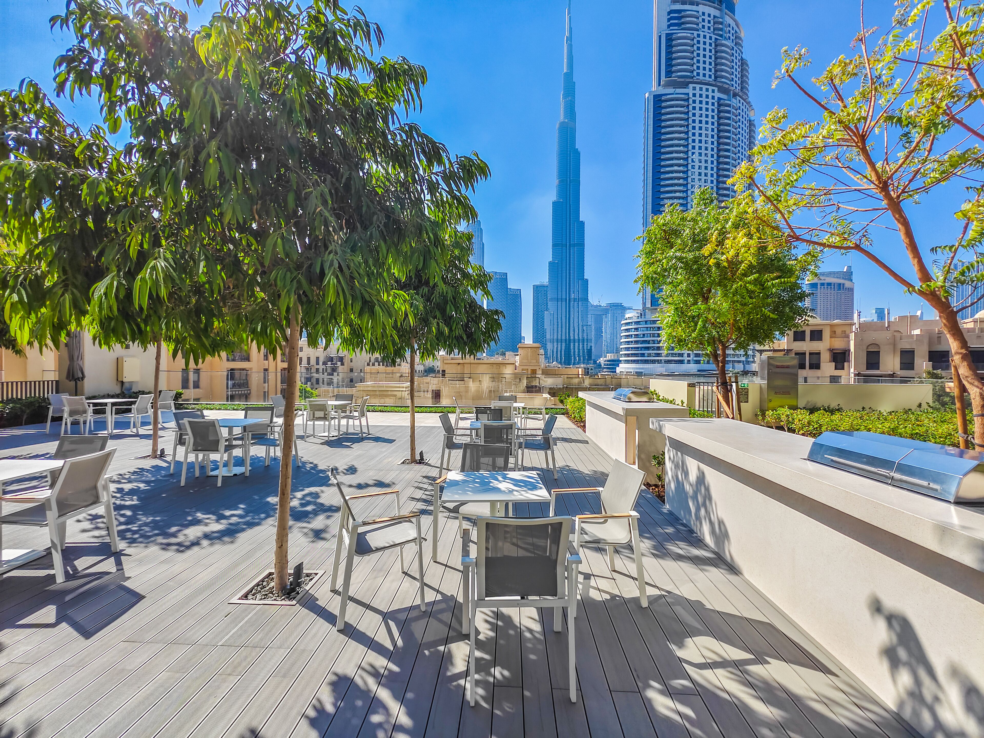 Un patio al aire libre con mesas y sillas, árboles y vistas del Burj Khalifa.