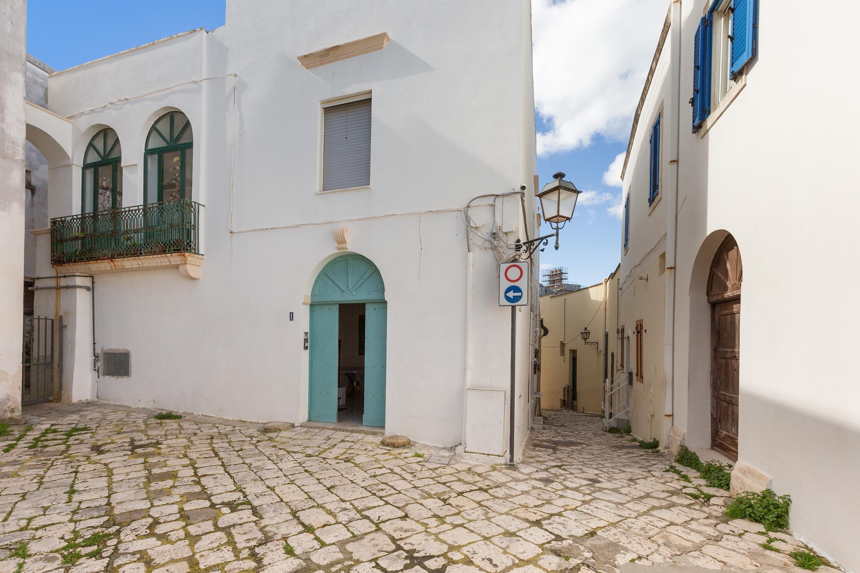 A cobblestone street with white buildings, a blue door, and a no parking sign.