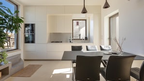 A modern kitchen with white cabinetry, a dining area with a black table and chairs, and a large window providing natural light.