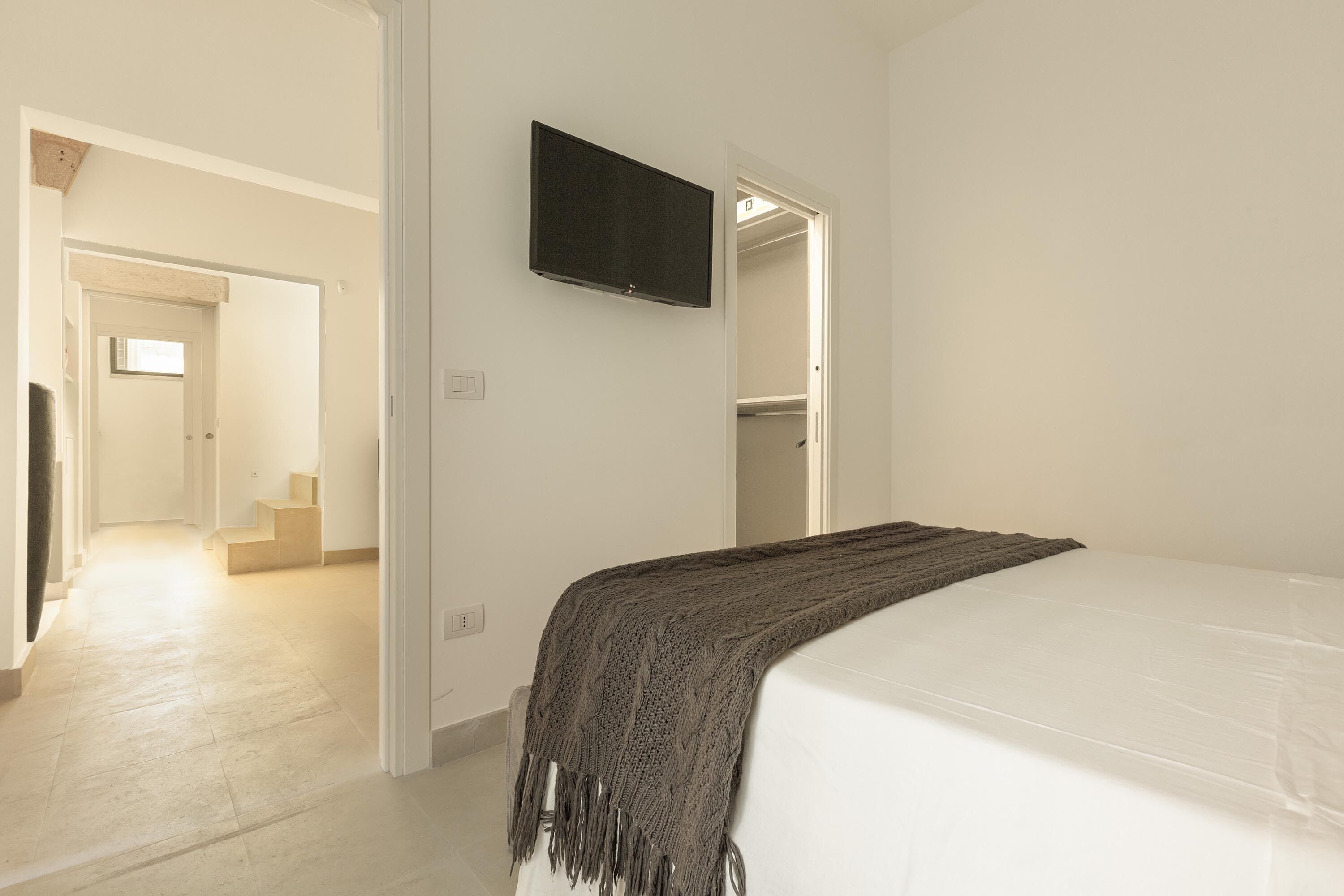 Un dormitorio con cama, televisor montado en la pared y una escalera que conduce a otra habitación.
