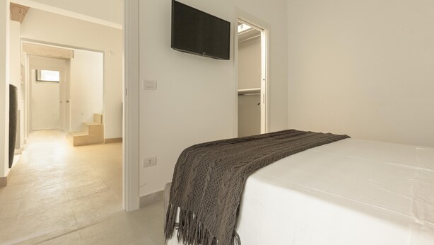 Una camera da letto con un letto, una televisione fissata al muro e una scala che conduce a un'altra stanza.
