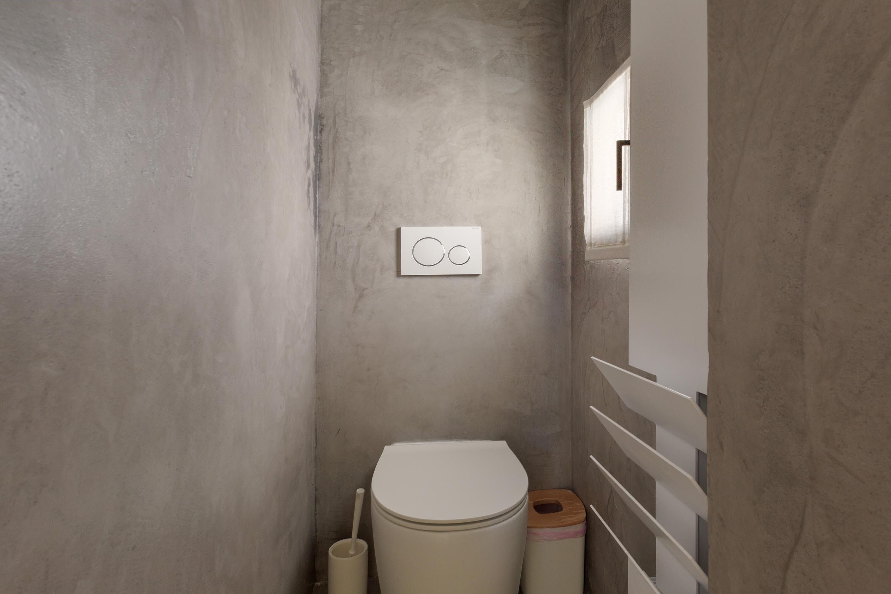 Un baño pequeño y moderno con inodoro, escobilla y cubo de basura.