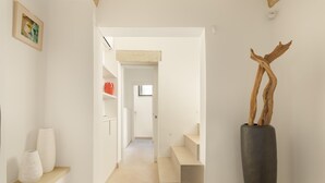 A hallway with a modern design, featuring a staircase, a large vase with a branch, and a framed picture on the wall.