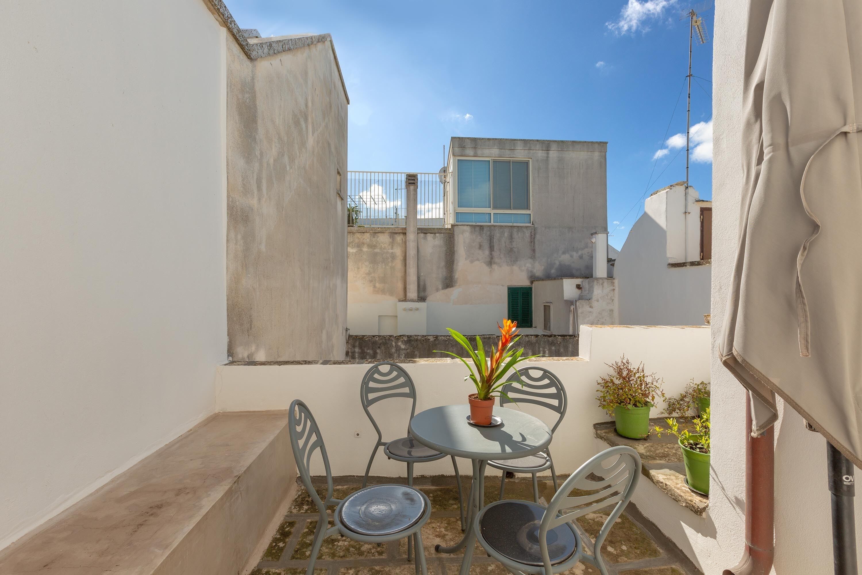 En hyggelig udendørs terrasse med et bord, stole, en potteplante og udsigt til omkringliggende bygninger.