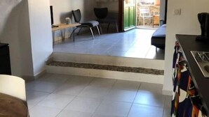 En rummelig stue med et tekøkken, et spisebord og udsigt gennem en bue til en udendørs terrasse.