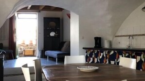 Et spiseområde med et træbord og hvide stole, et køkken med et mønstret backsplash, samt udsigt til det fri.