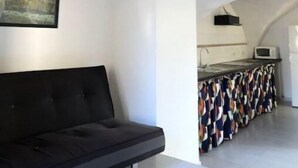 Et moderne interiør med en sort sofa, en rød lampe, et indrammet landskabsmaleri og et køkkenområde med en mikrobølgeovn.