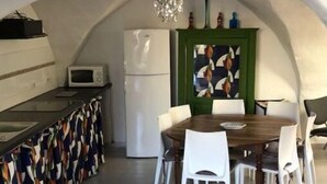 Et køkken med spiseplads under hvælvet loft, med mikrobølgeovn, køleskab og et kunstværk i grøn ramme.