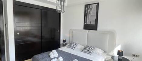 Habitación de hotel moderna con una cama grande, un armario negro, una mesita de noche con lámpara y un cuadro enmarcado en la pared.