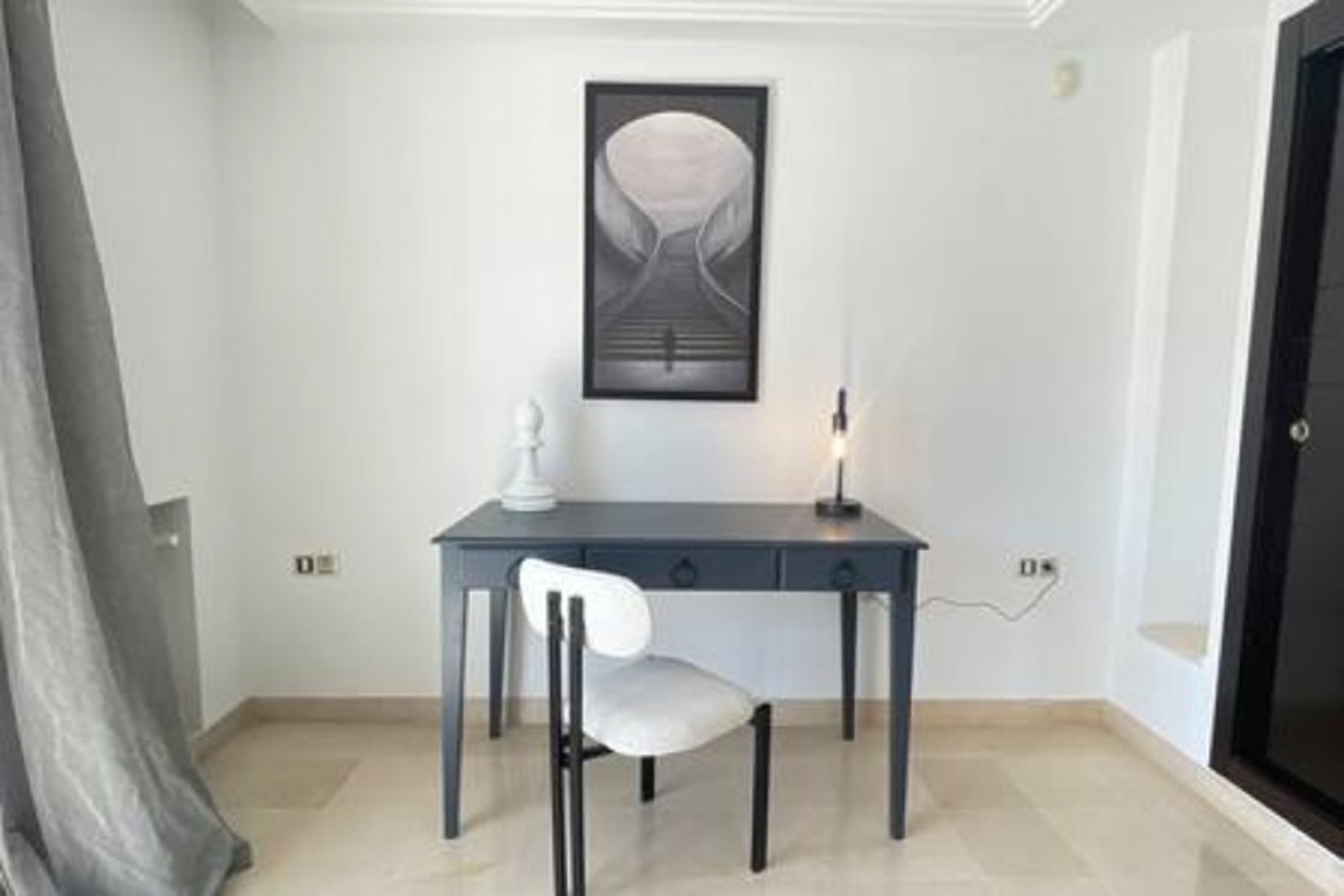 A room with a desk, chair, and a framed artwork on the wall.