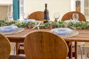A wooden dining table set with plates, glasses, and a bottle of wine, decorated with greenery and starfish. - Sardinia Re - Malta 29 Apartment (Alghero)