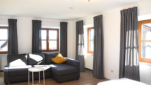 Een moderne woonkamer met een grijze bank, een kleine witte tafel en een bed met ruitbeddengoed.