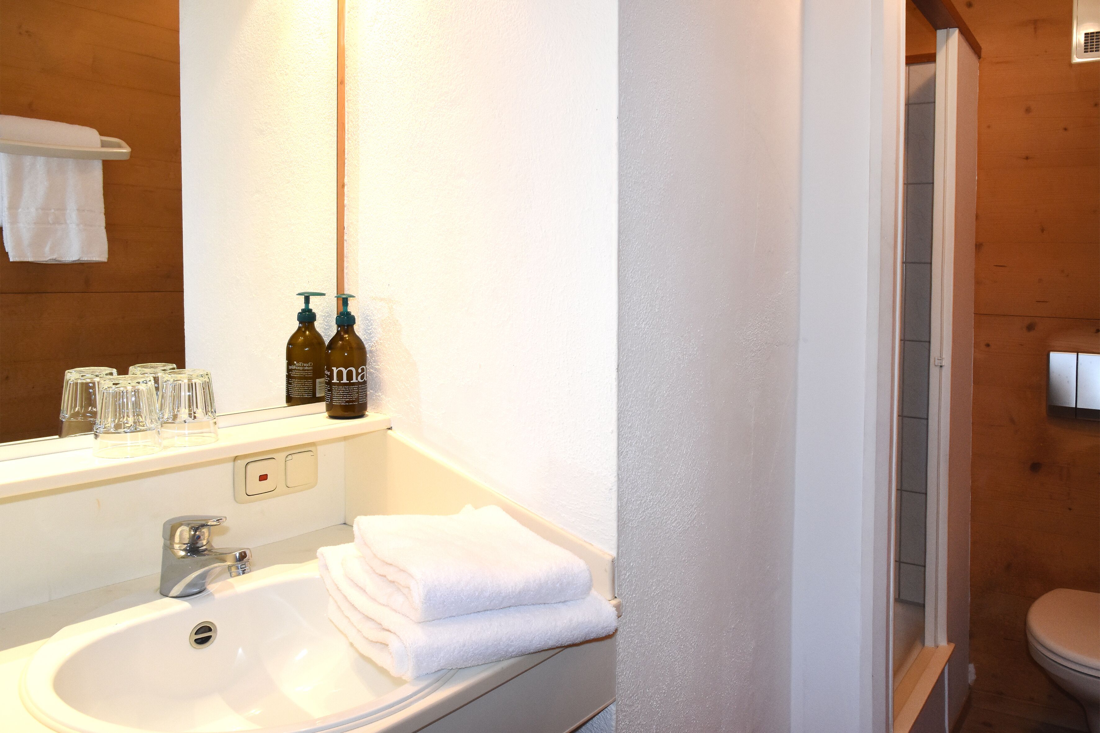 Un bagno con un lavandino bianco, uno specchio e un box doccia in legno.