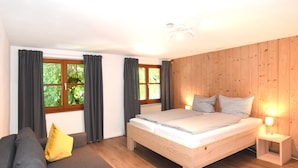 Een slaapkamer met een houten bed, een grijze bank en een raam met gordijnen.