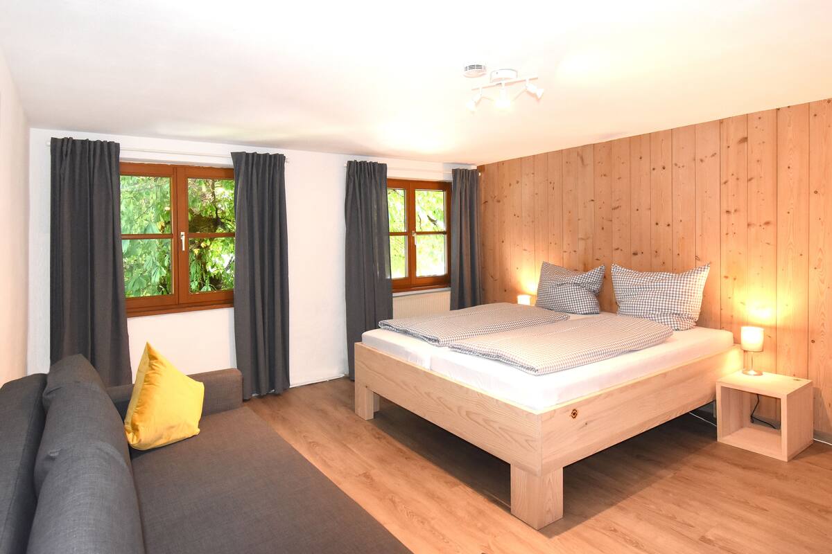 A bedroom with a wooden bed, a grey sofa, and a window with curtains.