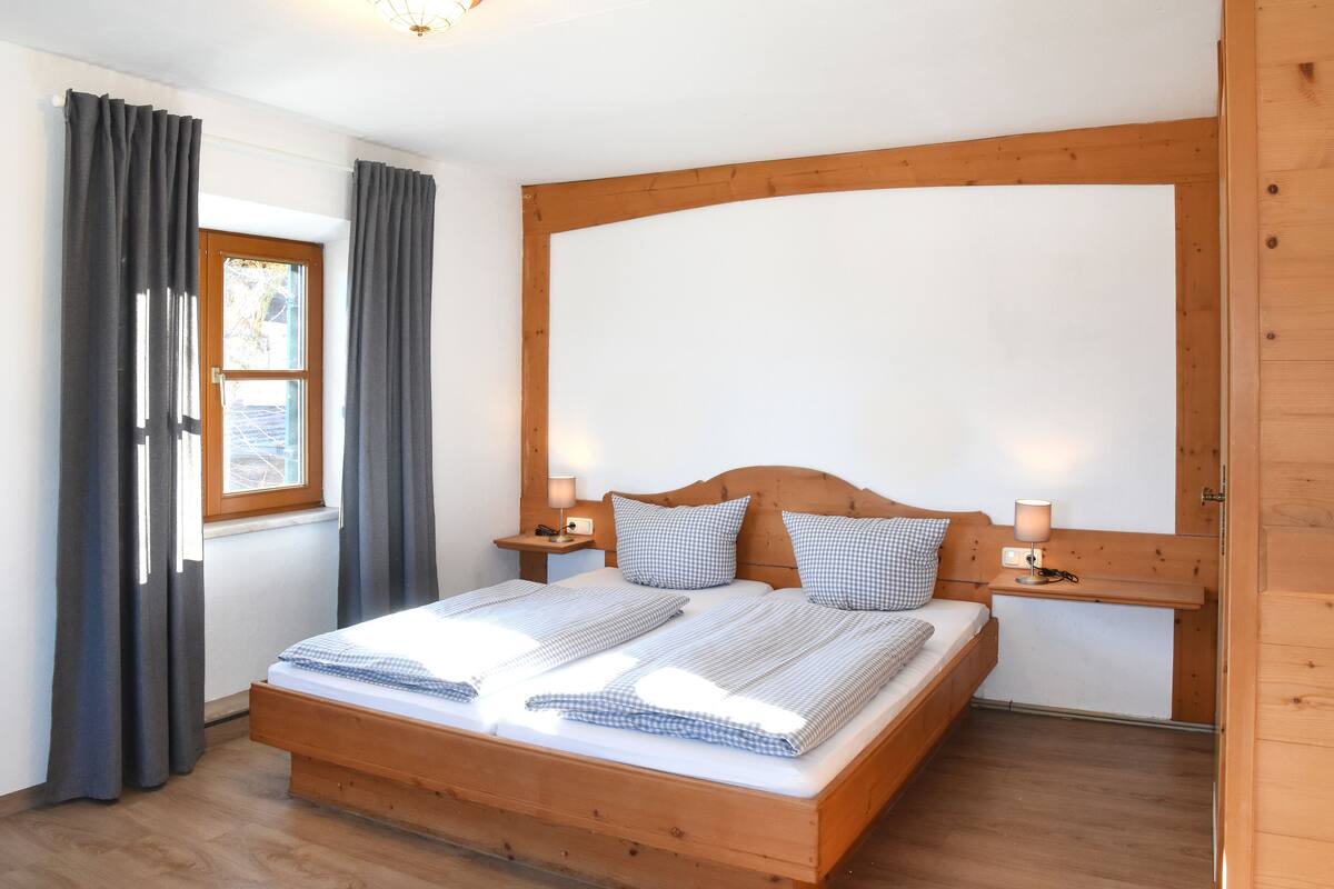 A wooden bed with a headboard, two bedside tables with lamps, and a window with curtains.