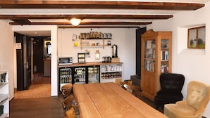 Een houten eettafel met stoelen, een zwarte en een beige fauteuil, en een kast met glazen deuren.