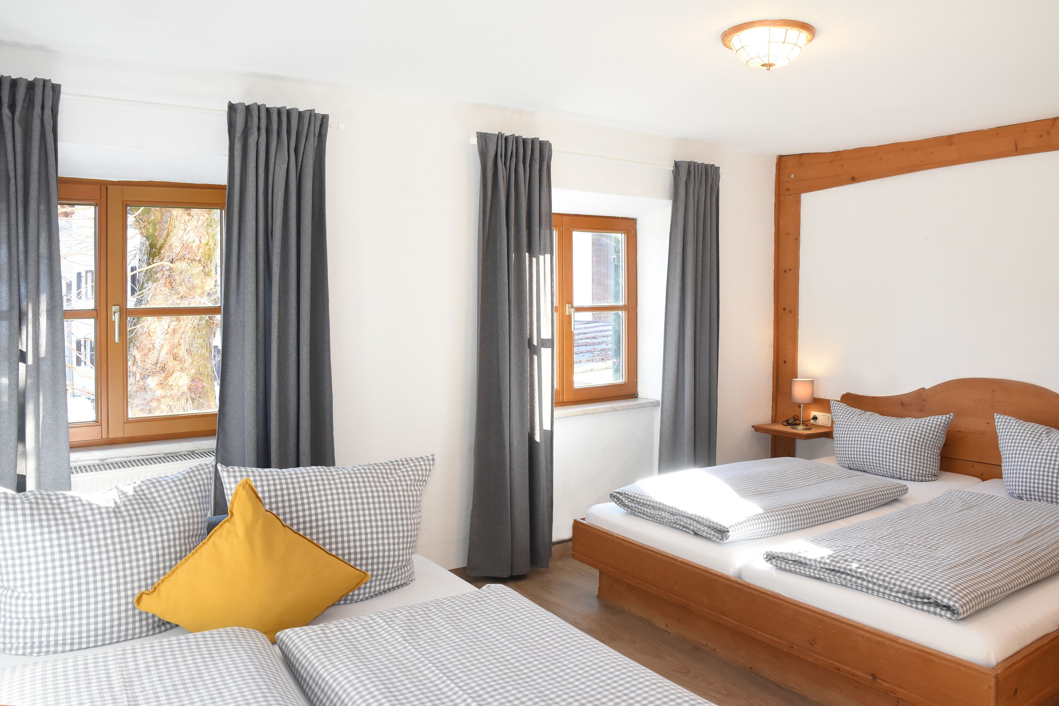 Un dormitorio con dos camas, cortinas grises, un cabecero de madera y una mesita de noche con una lámpara.