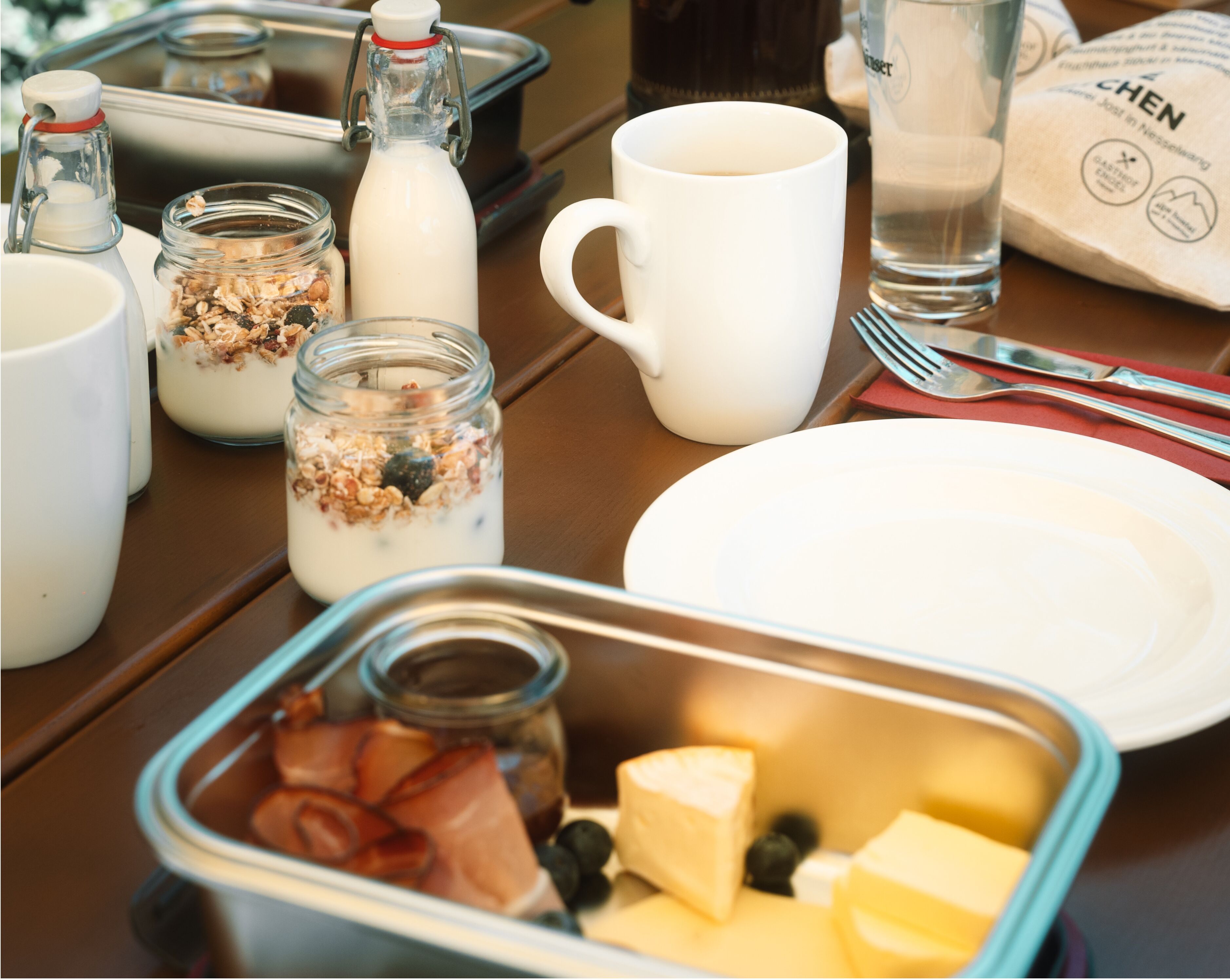 Un desayuno con diversas opciones de comida, como yogur, granola, queso y frutas, dispuestas sobre una mesa.