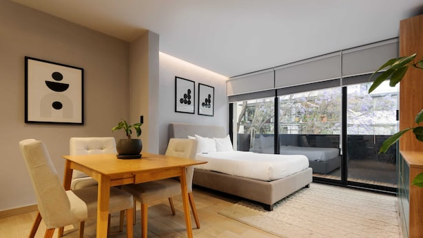 A modern bedroom with a sofa bed, a dining table with chairs, and a large window with a view of trees and buildings. - w* | Captivating Loft with Terrace in Polanco (Ciudad de México)