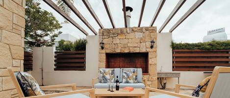 Un espacio al aire libre con chimenea de piedra, mobiliario de madera y vistas al horizonte de la ciudad.