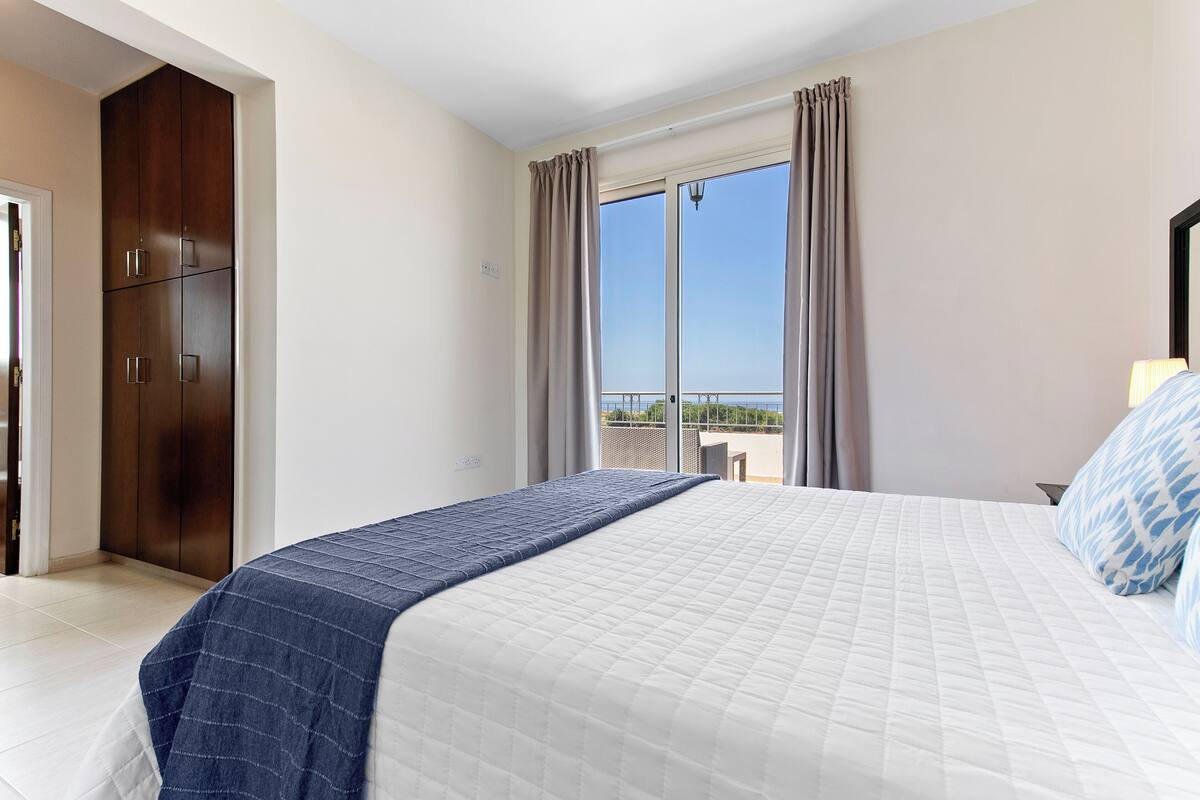 A hotel room with a bed, a wardrobe, a balcony with a table, and curtains.