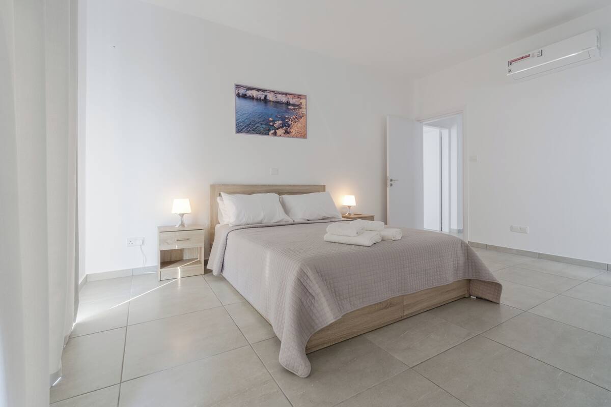 A modern bedroom with a bed, bedside lamps, a nightstand, and a painting on the wall.
