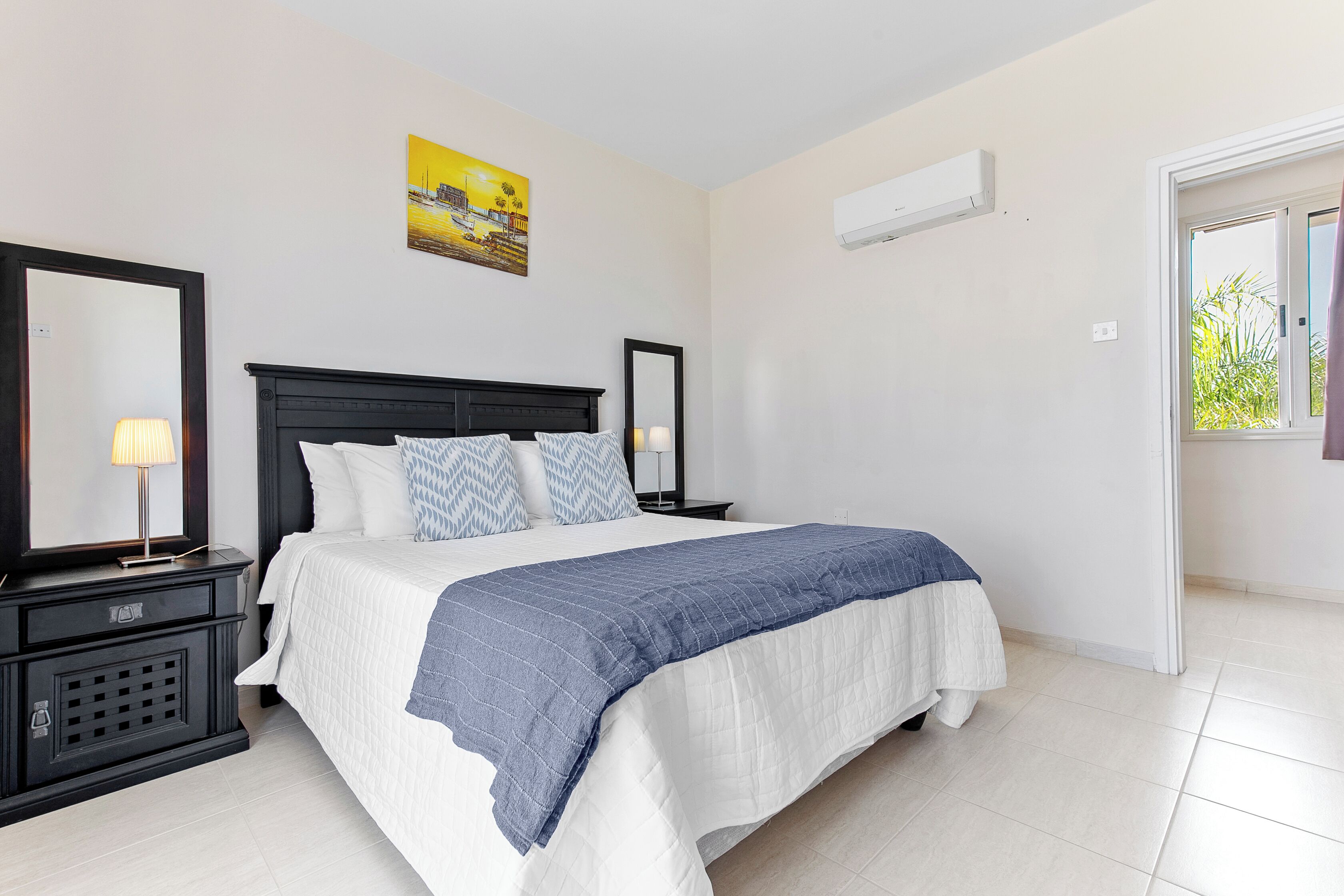 A bedroom with a bed, bedside tables, a mirror, and a painting on the wall.